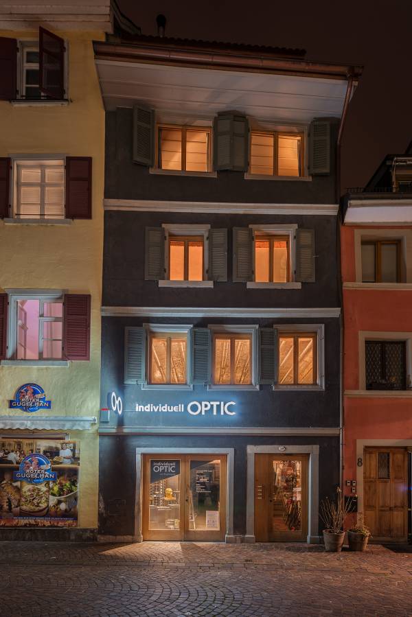 Das Dillschnitterhaus ist ein mehrst&ouml;ckiges Geb&auml;ude mit grauer Fassade und wei&szlig;en Fensterl&auml;den. Das Gesch&auml;ft 'individuell OPTIC' ist im Erdgeschoss sichtbar, mit beleuchtetem Schaufenster und einem modernen Logo.