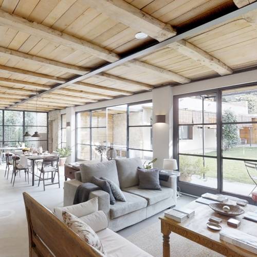 Lichtdurchfluteter Hotel-Loungebereich mit Sofas, Holztisch und gro&szlig;en Fenstern mit Blick auf Terrasse und Garten
