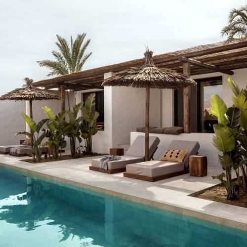 Hotelterrasse mit Pool, Liegen und Strohd&auml;chern, umgeben von tropischen Pflanzen