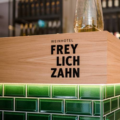 Holzschild mit der Aufschrift 'WEINHOTEL FREYLICHZAHN', platziert auf einer gr&uuml;nen Fliesenfl&auml;che.